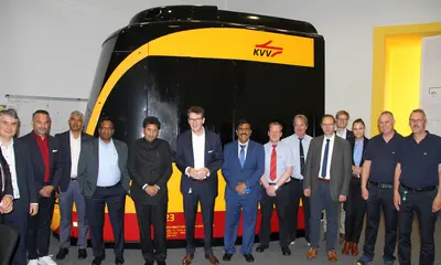 Die Delegation aus Indien und Vertreter*innen der VBK und AVG stehen vor einem Fahrsimulator, den die beiden Verkehrsunternemen beid er Ausbildung von neuem Fahrpersonal für ihre Tram- und Stadtbahnen einsetzten.