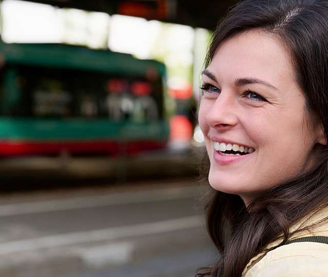 Eine junge Frau steht am Gleis und wartet auf die Bahn.