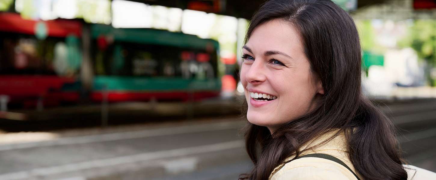 Eine junge Frau steht am Gleis und wartet auf die Bahn.