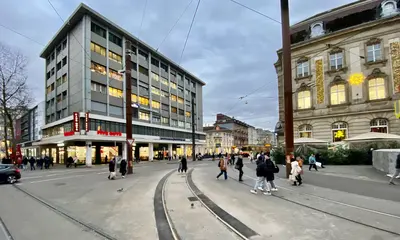 Das Foto zeigt den Gleisbogen am Karlsruher Europaplatz. Menschen überqueren die Kreuzung, im Hintergrund sind eine AVG-Stadtbahn und Häuserfassaden zu sehen.