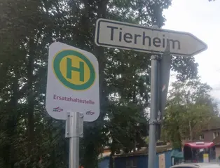 Das Foto zeigt zwei Schilder: Ein Schild, das auf die zusätzliche Haltestelle beim Tierheim Daxlanden hinweist. Danaben ist ein weißes Schild zu sehen, das den Weg zum Tierheim weist