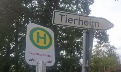 Das Foto zeigt zwei Schilder: Ein Schild, das auf die zusätzliche Haltestelle beim Tierheim Daxlanden hinweist. Danaben ist ein weißes Schild zu sehen, das den Weg zum Tierheim weist